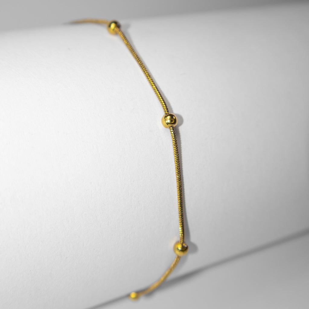 Detail of small gold beads evenly spaced along a fine chain bracelet
