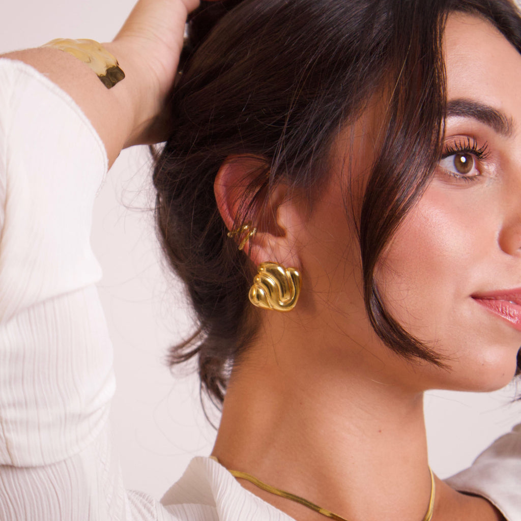 Model wearing sculptural gold statement earrings with a modern organic design
