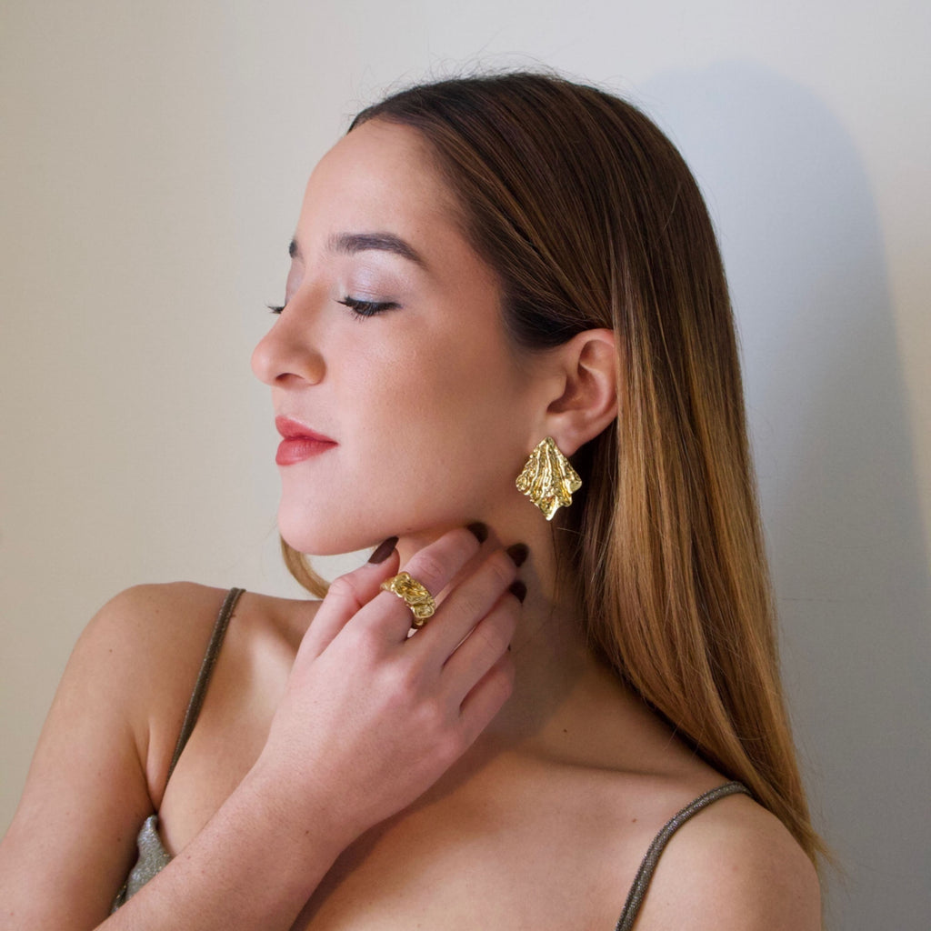 Gold statement earrings worn on ear with sculptural textured finish
