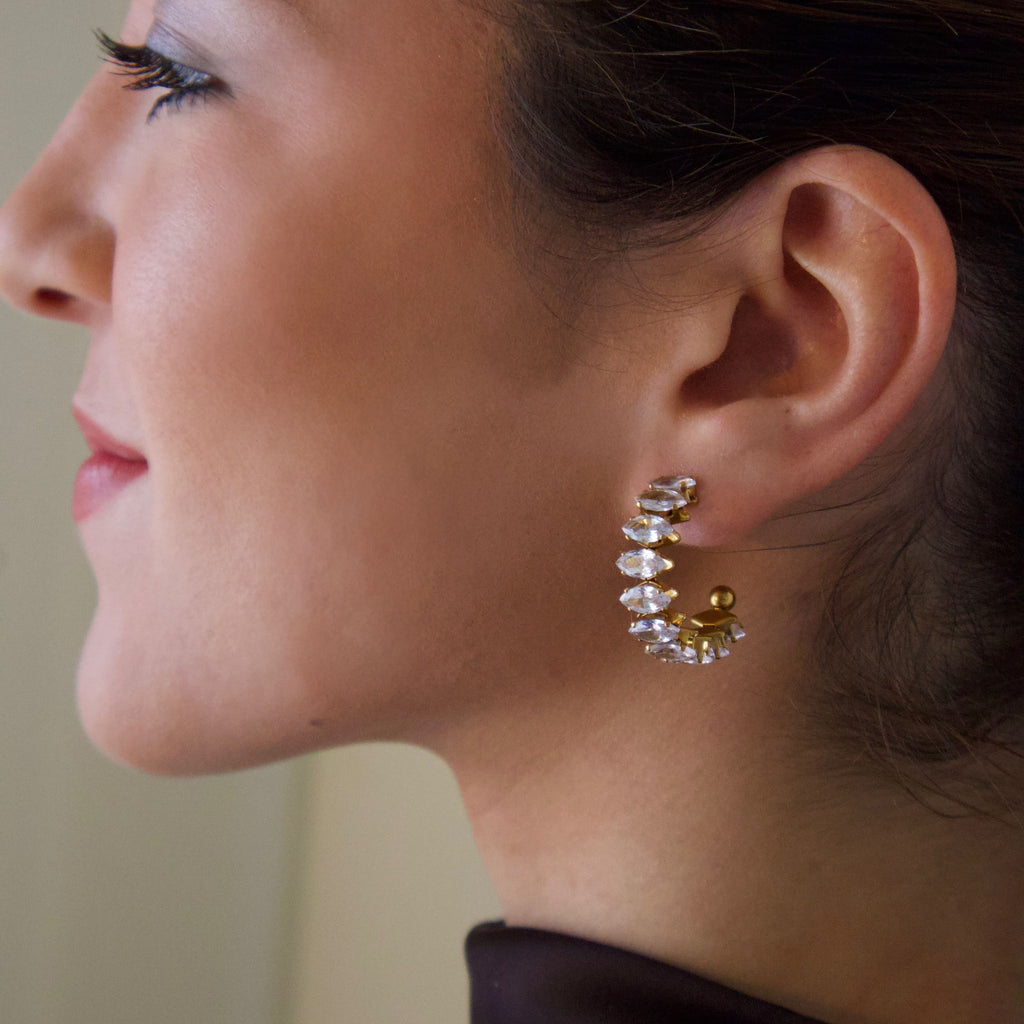 Gold hoop earrings featuring clear crystals arranged in a sculptural curved design
