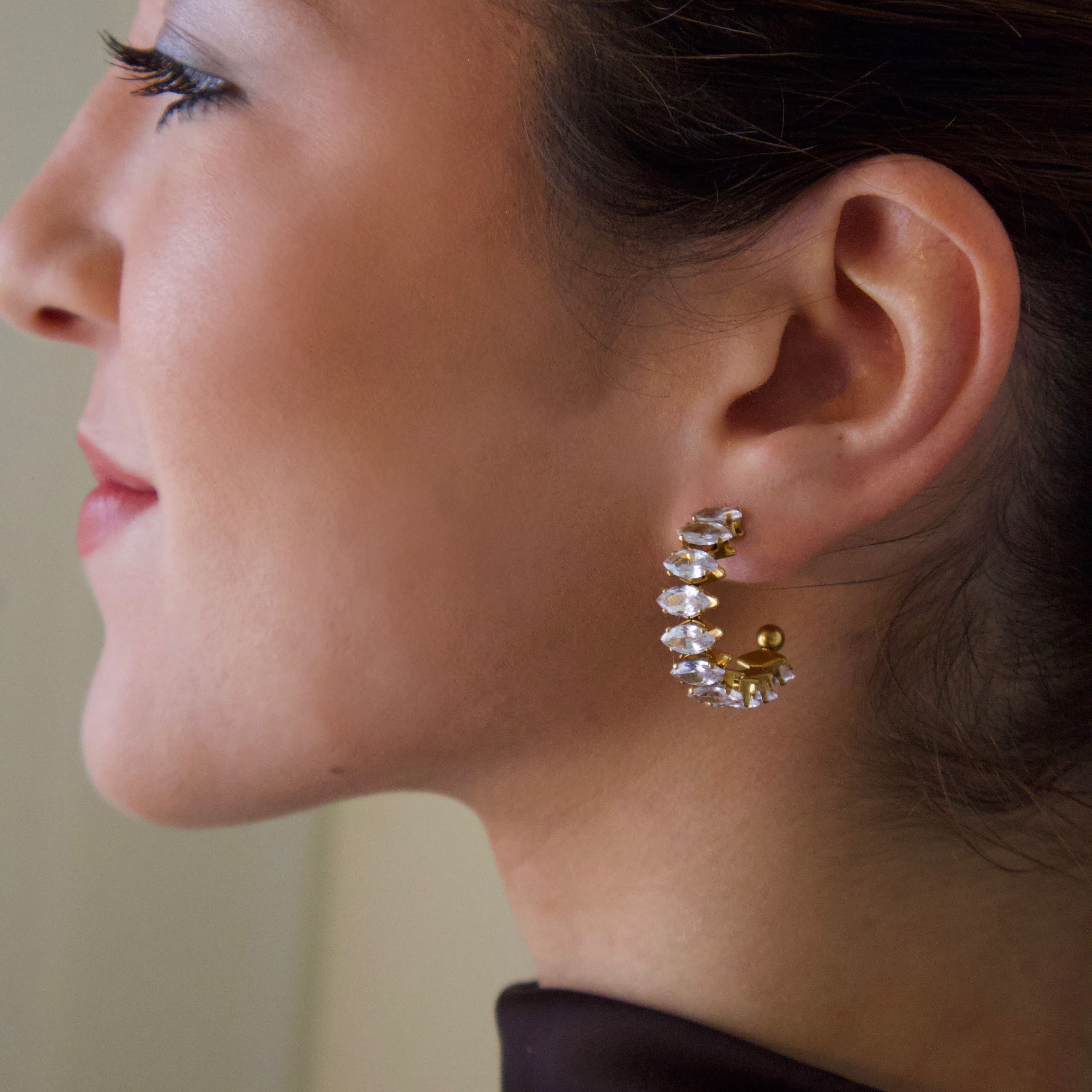 Gold hoop earrings featuring clear crystals arranged in a sculptural curved design

