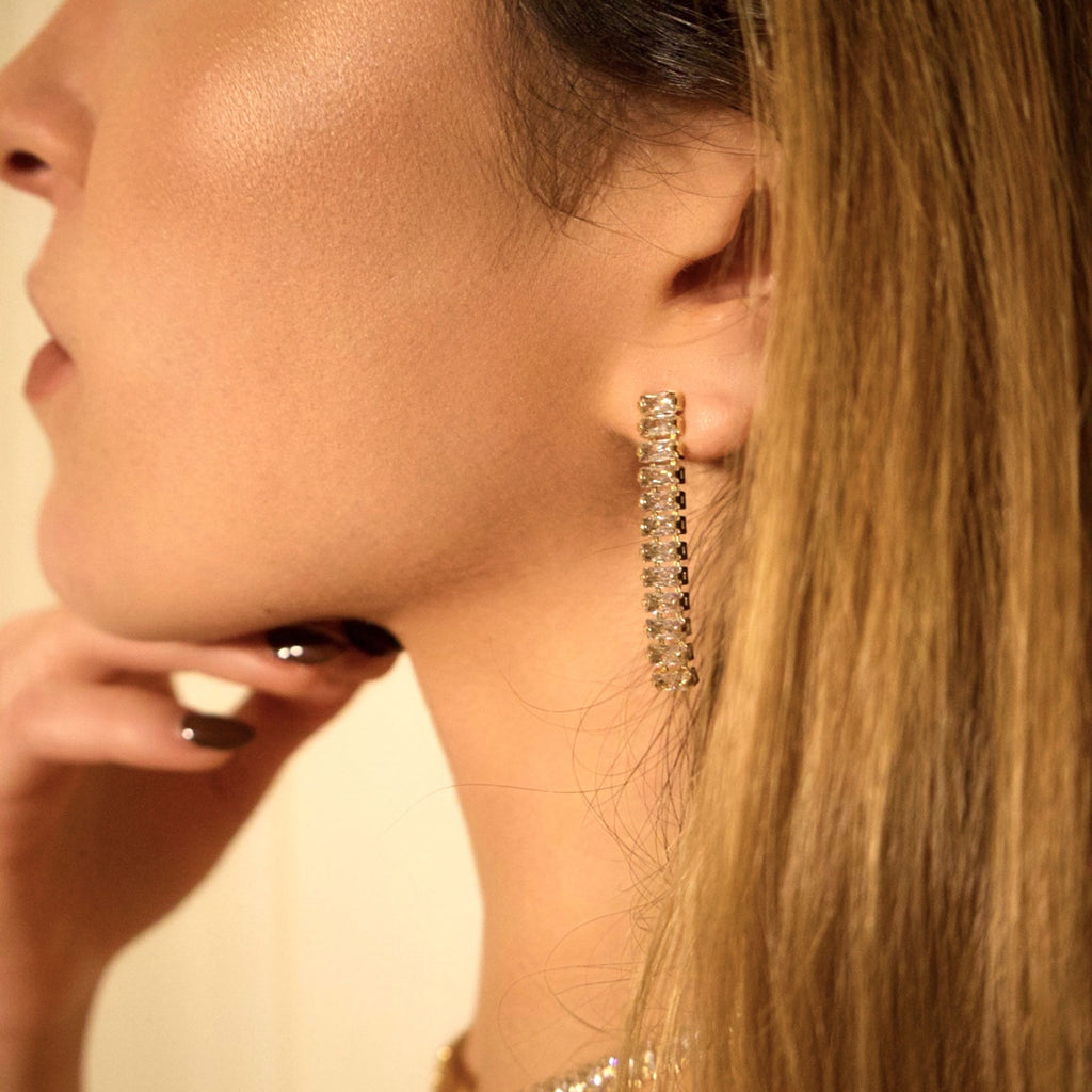 Long gold drop earrings with crystal details worn on the ear
