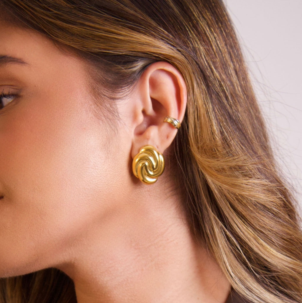 Organic gold stud earrings worn on the ear with sculptural swirl design

