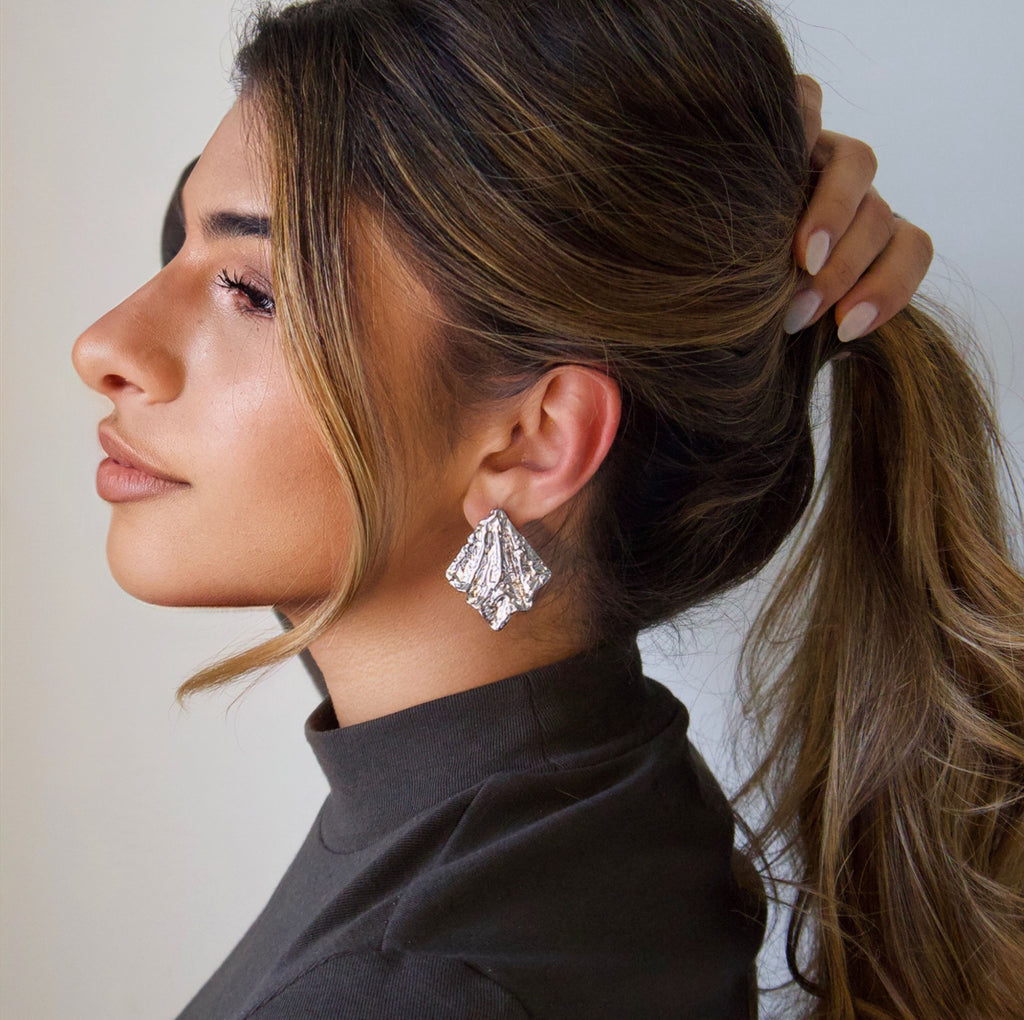 Silver statement earrings worn on ear with sculptural textured finish
